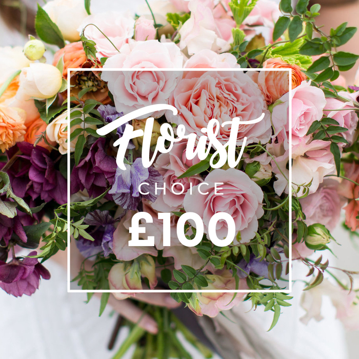 A richly textured, hand-tied bouquet is photographed close-up, offering a study in soft pastels and deep, grounding tones: multiple broad, ruffled pink garden roses dominate, their many petals folded like delicate fabric, while deeper plum-hued hellebore-like blossoms punctuate the lower left, lending shadowed contrast. Pale purple-and-white sweet peas weave through the blooms with featherlight movement, and warm peach-coral ranunculus provide layered, cup-like shapes that glow against creamy white filler flowers. Lush green foliage - a mix of trailing tendrils and broader, satiny leaves - cushions and frames the flowers, giving the design its garden-fresh, slightly wild aesthetic. Over the centre of the image sits a neat white square frame containing elegant script that reads Florist Choice, the subtitle CHOICE in smaller block letters beneath, and a large, bold ?100 displayed clearly at the bottom, signalling a florist-selected premium option. A gentle pair of hands supports the bouquet at the stems, a faint pale sleeve visible and the background softly blurred to hold focus on texture, colour and craftsmanship. The composition conveys romance, quality and intentionality; it is the sort of arrangement a Queensbury customer might choose for milestone birthdays, grateful thank-you gifts, or intimate weddings, where expert selection of seasonal blooms creates a memorable, heartfelt impression.