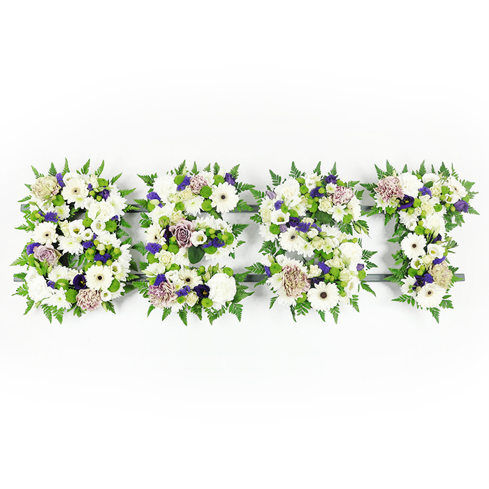 An overhead composition shows the word BEST rendered in four bold floral letters, each a careful study in white blooms, soft mauves, and verdant greenery set cleanly against a bright white background. Large pristine white Gerbera daisies with their darker centres sit prominently alongside delicate white lisianthus and full, ruffled carnations, creating layers of petal shapes from broad disks to soft, billowing cups. Pale mauve and lavender roses and lightly tinged carnations thread through the arrangement, their subtle tones introducing a reverent warmth, while tiny clusters of deeper purple filler add depth and a measured, respectful contrast. Around every letter, feathery fern fronds form a soft, living border, their airy texture both framing and cushioning the flowers; small green button chrysanthemums are sprinkled within the letters for fresh, compact pops of colour and density. The florist's structural base is a dark grey or black form that peeks through in places, providing the precise edges that keep each letter legible in a funeral setting. Executed with the same care we bring to memorial pieces delivered locally, this tribute is the sort of personalised floral message families ask for when arranging services in Queensbury and the surrounding NW London community. At Flower Delivery Queensbury we consider scent, texture, and sight together: the cool sweetness of white petals, the soft perfume of mauve roses, and the reassuring geometry of the lettering combine to create a dignified, heartfelt expression of remembrance.