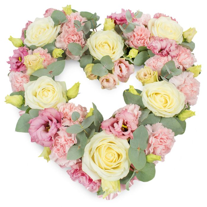 This image shows a beautifully crafted, heart-shaped funeral wreath presented on a crisp white background, the flowers so closely arranged that the entire heart appears plush and full. Dominating the design are several large cream and pale yellow roses, each one carefully opened to reveal layers of velvety petals, their centres swirling in soft, spiralling patterns. These roses are placed at balanced intervals to define the structure of the heart, suggesting purity, devotion, and quiet admiration. Between and around them, light pastel pink carnations fill the gaps, their ruffled, feathery petals creating gentle shadows and texture that soften every edge. Deeper pink to mauve lisianthus blooms are threaded throughout, their more open, cup-like shapes offering contrast to the tight roses and frilled carnations, while their slightly darker tones add depth and visual warmth. Small yellow-green buds are visible in the mix, conveying freshness and the sense that some stems are only just beginning to unfurl. Silvery-green eucalyptus leaves weave through the entire tribute, their round and oval leaves overlapping delicately and tracing the outer line of the heart, bringing calm, cool tones and a fragrant, herbal note. The wreath feels both luxurious and serene, a design that would sit gracefully at a funeral or memorial service in Queensbury, perhaps near Stag Lane or close to the local crematorium. Crafted with the care you would expect from a neighbourhood florist, this heart arrangement offers a gentle way for families in Queensbury to express sympathy, remembrance, and enduring love for someone dearly missed.