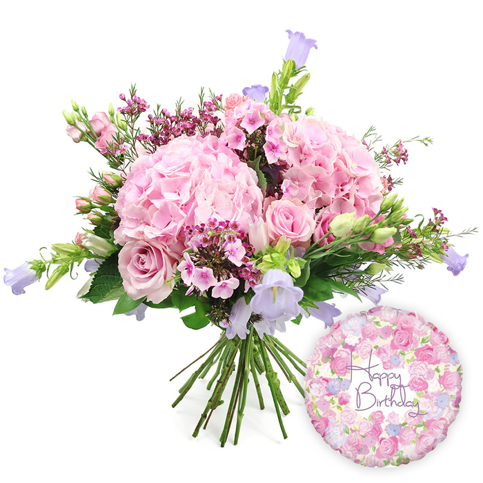 A beautifully coordinated birthday gift set is captured against a luminous white background, featuring a hand-tied bouquet of pink and purple blooms paired with a festive foil balloon. The bouquet dominates the scene, its rounded shape filled to the brim with large, fluffy hydrangea heads in a gentle blush pink tone. Each hydrangea cluster is made up of countless small petals that overlap to create a sumptuous, cushiony texture, evoking the softness of early summer blossoms in gardens around Queensbury. Nestled among these hydrangeas are light pink roses, some elegantly unfurled to reveal their classic spirals, others still in compact bud form, suggesting the promise of continued blooming once the bouquet reaches its new home. Interspersed throughout the design, tiny clusters of deeper pink or magenta filler flowers, reminiscent of waxflower, lend intricate detail and a lively burst of colour, like confetti scattered between the larger blooms. Rising delicately above and between the flowers are campanula stems, their bell-shaped blossoms in soft lavender and periwinkle offering slender vertical accents and a cool counterpoint to the warm pinks. A generous collar of fresh greenery frames the blossoms-broad leaves and finer stems arch around the flowers, adding depth and a fresh-from-the-market feel, as though gathered that morning from a trusted supplier near Queensbury's local shops. The natural stems at the base are clearly visible, tightly gathered in the traditional hand-tied style for easy placing in a favourite vase. To the lower right, a shiny round Mylar balloon completes the celebratory composition. Its surface is decorated with a delicate all-over floral motif in pinks, creams, and lavenders, and in its centre the phrase Happy Birthday is scripted in rich purple lettering, making the image an ideal visual for birthday flower delivery across Queensbury and nearby neighbourhoods.