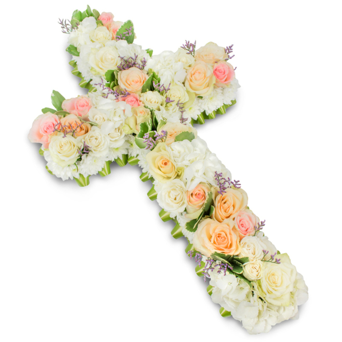 A refined and graceful cross-shaped floral tribute is photographed against a crisp white studio background, allowing every soft colour and texture to stand out with clarity. The cross has gently rounded edges and a substantial, almost pillow-like volume, created by a dense covering of fresh blooms. At its heart are numerous white and ivory roses, some fully open and others just beginning to unfurl, their silky petals overlapping in concentric layers. These classic roses form the main structure of the design, guiding the eye along the vertical and horizontal arms of the Christian cross. Surrounding and supporting them, clusters of white hydrangea and similarly dense white blossoms fill the spaces, giving the arrangement a plush, cloud-soft appearance. Intertwined among the white flowers are delicate accents of colour: pale peach roses, apricot-tinged buds, and light blush pink roses appear in thoughtful groups, like gentle highlights that lend comfort and warmth to the tribute. Fine touches of lavender or light purple filler flowers are dotted sparingly throughout, adding a subtle, almost ethereal contrast that enhances the overall intricacy without breaking the serene mood. At the outer edges, glimpses of fresh green foliage peek through, framing the floral surface and giving the cross a natural outline, as if it were freshly gathered from a peaceful garden. The lighting is even and luminous, casting a soft shadow beneath the arrangement and emphasising its three-dimensional presence. This floral cross, reminiscent of the calm residential streets and quiet green spaces around Queensbury, feels like a dignified funeral or memorial piece, meant to convey sincere sympathy, spiritual comfort, and the lasting remembrance of a life cherished by family and friends.