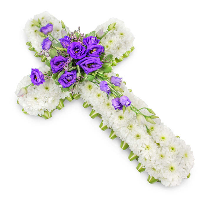 A reverent floral cross tribute is displayed against a flawless white background, reminiscent of a calm chapel interior in Queensbury on a quiet weekday afternoon. The cross is entirely composed of tightly packed white spray chrysanthemums, their petite, rounded heads forming a continuous blanket of bloom. The chrysanthemums' faint green centres punctuate the white, creating a delicate, almost lace-like texture across the surface. Along the perimeter of the cross, a bright lime-green ribbon runs in a clean, uninterrupted line, crisply framing the design and adding a vivid, botanical accent that emphasizes the symmetry of the shape. At the heart of the cross, where the horizontal and vertical arms intersect, rests a generous cluster of deep purple lisianthus flowers. Their layered petals, saturated in tones of royal purple and plum, rise above the white base, drawing the eye to this central point of reflection. Intertwined among them are sprigs of soft, light green foliage and a scattering of small filler flowers, adding depth and a natural woodland touch. From this focal cluster, additional lisianthus blooms and buds trail thoughtfully downwards along the vertical arm, forming a gentle, diagonal sweep that suggests a flowing ribbon of remembrance. The piece is photographed from a slightly raised angle, with a subtle shadow cast beneath that makes the cross appear as if it is resting lightly upon a pristine surface. Ideal for a funeral service held in a local Queensbury church or for delivery to a nearby crematorium chapel, this floral cross expresses sympathy, faith, and enduring love in an understated yet deeply meaningful way.