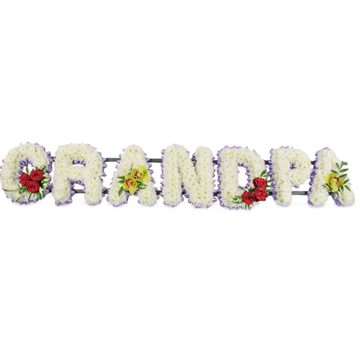 The image shows a carefully composed floral tribute spelling out GRANDPA in large, block-style letters, presented horizontally so that the name reads clearly from left to right against a clean, uncluttered white background. Each letter is constructed on a sturdy, unseen frame and then completely covered with tightly packed white chrysanthemums, giving the surface of the design a smooth, velvety appearance with just a hint of individual petal detail. A slim border of soft lavender-purple ribbon runs neatly around the outline of each letter, providing definition and a gentle hint of colour that enriches the overall composition without overwhelming its simplicity. Colour accents are thoughtfully placed to add character and meaning. In the curve of the opening G, a small but striking cluster of deep red roses is framed by fresh greenery, symbolising deep familial love. A little further along, the first A is adorned with graceful yellow-green orchids, their unusual form and touches of warm reddish colouring suggesting admiration and the uniqueness of the person remembered. The rounded D echoes the G with a matching cluster of red roses, maintaining visual balance, while the final A carries another spray of the same orchids, softly tying the design together. The letters are subtly joined from behind by horizontal bars that ensure the entire word sits straight and secure as one complete piece. This floral lettering, often chosen by families around Queensbury for funeral services, crematorium chapels, or graveside tributes, conveys a message of affection, respect, and gratitude for a beloved grandfather in a way that feels understated yet deeply heartfelt.