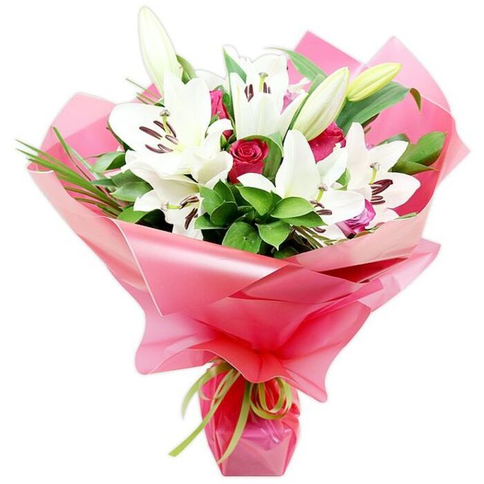 This photograph shows a striking, hand-tied bouquet designed around a dramatic contrast of colour and texture: pristine white lilies towering above a cluster of deep red roses, all framed by generous greenery and bright pink wrapping. The white Oriental lilies are abundant and full, their trumpet-like blooms opening wide to reveal silky petals that form gentle curves and points, each bloom centred by a trio of dark, rust-coloured anthers that hover over the petals like fine brushstrokes. A few lilies are still enclosed in pale green buds, their tapered forms standing upright and adding a sense of anticipation and height. Tucked among these commanding flowers are red roses in various bud stages, from very tight, almost spherical forms to slightly opened blooms showing intricate whorls of velvety petals. The roses' rich ruby tones provide a powerful contrast to the lilies' cool whiteness, creating a visual rhythm of light and depth. Surrounding the blooms is an assortment of deep green foliage: some leaves are broad and glossy, catching reflections, while others are long and slender, arching gracefully and lending the arrangement a more natural, garden-like feel, reminiscent of the mature shrubs and hedges seen in Queensbury's quiet cul-de-sacs. The stems are wrapped in a wide band of shiny, translucent bright pink cellophane, gathered into soft folds that shimmer under the light, giving the bouquet a celebratory aura. At the very base, a fine lime green ribbon is tied snugly, its delicate sheen offering a crisp contrast to the pink wrapping. The composition feels both modern and timeless, ideal for marking special occasions, anniversaries, or thoughtful same-day deliveries to homes and offices throughout the Queensbury area.