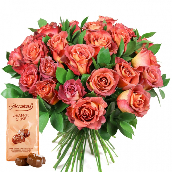 Dominating the scene in this vibrant composition is an opulent bouquet of roses, each bloom artfully arranged to reveal a stunning bi-colour display reminiscent of late summer evenings in Queensbury. The bouquet, placed against an unblemished white background, overflows with lush, open roses whose petals gently transition from warm peach and honeyed yellow at their tight centers to deep coral and sultry pink on the outer edges, creating a mesmerising ombre effect. Frothy bundles of dark green foliage-most likely ruscus or polished salal-thread between the roses, injecting breath and vitality into the arrangement and lending the entire set a sense of depth and expertly styled abundance. Anchoring this visual celebration in the lower-left foreground is a light, cream-toned bag of Thorntons Orange Crisp chocolates, standing upright, its elegant branding and boldly written name 'ORANGE CRISP' immediately catching the eye. Below the enticing product illustration, two real chocolates are placed, their smooth, glazed surfaces gleaming, betraying the rich, orange-infused truffle and crisped wafer hidden within. The bouquet's fresh stems peek neatly below, suggesting the bouquet has been hand-tied by a skillful florist just off Queensbury Station. The overall tone is one of lavish care and refined indulgence, perfect for honouring mother figures, romantic moments, birthdays, or any memorable day that calls for an especially thoughtful gift. Every detail sings with the artistry and community spirit that defines flower delivery throughout Queensbury and its leafy nearby avenues.