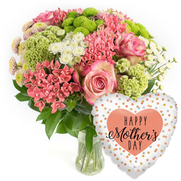 A joyful Mother's Day floral gift is photographed in studio lighting against a spotless white background, highlighting every colour and texture as if it were ready to go out on a same-day delivery run through Queensbury. The bouquet is arranged in a clear, cylindrical glass vase, where straight, neatly cut stems are visible through the water, giving a sense of freshness and professional care. Above the vase, the flowers form a lush, rounded canopy of pinks, corals, greens, and whites. Several large pink roses command attention, each bloom unfurling velvety petals that deepen in colour toward the edges, like a soft blush caught at dusk. Nestled among them are numerous small, coral-pink clusters reminiscent of kalanchoe or similar compact florets, providing a warm, lively accent that brings the arrangement to life. Lime-green button chrysanthemums stand out with their distinctive, textured domes, almost frilly at the surface, adding a contemporary twist and a lively contrast to the softer hues. Threaded through this mix are white daisy-like spray chrysanthemums, their crisp petals and sunny centres lending brightness and a pleasant, garden-fresh feel, as though picked from a border not far from Queensbury Station. Rich, dark green foliage surrounds and supports the blooms, filling out the shape and giving a sense of depth and abundance. To the lower right of the bouquet, a glossy heart-shaped foil balloon completes the gift. Its light background is sprinkled with shimmering gold and peach-silver dots, while a bold peach heart in the centre frames the words HAPPY Mother's DAY in elegant black script. Together, the bouquet and balloon create a warm, celebratory tableau that beautifully captures appreciation for mums in the Queensbury area.