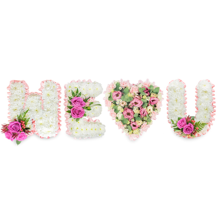 This elegant floral statement spells H E (heart) U across a crisp white field, a composition that feels both intimate and ceremonially poised. The capital letters H, E and U are each formed from tightly packed white chrysanthemums, their small daisy-like petals creating a plush, serene surface reminiscent of freshly fallen snow. A soft blush-pink satin ribbon traces the outer edges of every character, its slight ruffle adding a tender, almost fabric-like softness to the botanical shapes. Small, dramatic accents of fuchsia-pink roses punctuate the arrangement-one cluster grounds the left side of the H, a second bright trio adorns the E's centre bar, and a final duet of roses nestles within the inside curve of the U-each accompanied by glossy, deep-green ferny foliage and occasional reddish-pink berries that add a restrained pop of seasonal colour. The central heart, standing in place of a single letter, is deliberately more textured and varied: pale pink carnations and spray carnations form the bulk, interspersed with delicate blush lisianthus or miniature roses and open pockets of pale green eucalyptus leaves that breathe cool freshness through the composition. The eucalyptus provides a subtle aromatic lift, the carnations add soft ruffles under the hand, and the ribbons lend a cohesive, sentimental finish. Seen as a whole, the piece conveys a quiet statement of love and remembrance, suitable for a memorial or a romantic gesture; its craftsmanship reflects the practised hands of local florists familiar with Queensbury and neighbouring enclaves such as Kingsbury and Harrow, where such personalised tributes are often asked for at services or home gatherings.