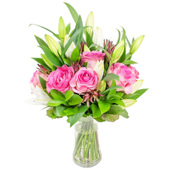 An elegant, fresh-cut bouquet of deep pink roses and poised white lilies rests in a crystal-clear glass vase on a pristine white backdrop, the composition pared to its most charming elements. The roses are the stars here-large, fully opened blooms whose velvety petals layer from soft blush to vivid fuchsia, each petal edge soft and tactile in description. Sprinkled among them are white lily buds: some tight and elongated, others just beginning to unfurl their trumpets and hint at a subtle, powdery perfume. The arrangement is wrapped in abundant greenery, from wide, glossy leaves that give the bouquet structure to lighter, feathery sprigs that breathe, creating a natural dome of foliage. Tiny, darker burgundy or reddish-brown filler buds are woven through the greens, lending contrast and a textured counterpoint to the pastel blooms. The vase's slightly tapered silhouette reveals clear water and straight, neatly cut stems beneath, a sign of careful handling and freshness. Studio lighting reads bright and neutral, isolating each colour and texture so the bouquet photographs cleanly for catalog use or delivery listings. As a Queensbury florist I craft pieces like this for local moments-birthday surprises for neighbours near Queensbury tube, table-centrepieces for small celebrations in the Kingsbury Road area, or a thoughtful 'thank you' delivered across Wembley or Harrow. Available for local delivery through Flower Delivery Queensbury, it conveys warmth, celebration, and delicate floral artistry without fuss.