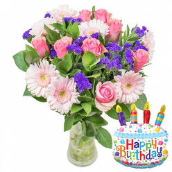 Bathed in gentle, clear morning light, this bouquet reads like a small celebration arranged by a neighbourhood florist familiar with Queensbury's quiet corners. At its centre sit dozens of soft pink roses, petals layered like silk and shifting from pale blush to a warmer pink toward their centers, giving the arrangement a feeling of quiet romance and tender joy. Around them, generous pink Gerbera daisies open wide with relaxed, rounded faces, their centres touched with a buttercream yellow that softens the palette. Interwoven are clusters of lively purple statice - crisp, textured sprays that bring depth and a subtle, wild charm - while glossy, thick green foliage provides a lush backdrop and frames every bloom with steady support. The clear glass vase reveals the green stems and clean water below, a small but tangible promise of freshness and careful handling. A whimsical cake-shaped Mylar balloon with white 'frosting', blue icing trim and rainbow sprinkles leans at the side; four slender candles in purple, red, orange and blue are painted on top, their tiny flames suggesting celebration without shouting, and the playful 'Happy Birthday' greeting echoes the bouquet's message of warmth. As a local florist, I imagine this arriving to a kitchen table near Queensbury Tube or delivered to a home off Kingsbury Road - a fragrant, tactile gift that smells faintly sweet like a summer garden and feels handcrafted by someone who knows how flowers comfort and delight. Flower Delivery Queensbury prepares arrangements like this for thoughtful birthday deliveries across the area.