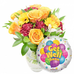 This cheerful 'Get Well Soon' gift pairing feels like a bedside visit from a close friend - a lush bouquet placed in a clear glass vase beside a gleaming Mylar balloon, photographed on a clean white backdrop that highlights colour and texture. The centerpiece is a generous grouping of large, opening roses in warm orange and deep yellow tones; their velvety petals unfurl in layered spirals and lend a soft, comforting scent. Bright yellow gerbera daisies punctuate the arrangement with sunny, almost playful faces, while rich maroon carnations add a plush, ruffled texture that grounds the palette. Light, white alstroemeria weave through the larger blooms, bringing delicate contrast and an airy, graceful line. A mix of glossy, verdant foliage cradles each stem and gives the bouquet a freshly-cut, just-arrived-from-the-market look-something familiar to locals who spot our van near Kingsbury Road and the Queensbury parade. Nestled at the lower right, a metallic round balloon catches the light; its silver field frames a cluster of illustrated balloons in purple, pink, blue, lime and yellow, some striped or spotted, and the central message "Get Well Soon" appears in bold yellow-and-blue letters with a soft shadow. Tiny starburst motifs and a small 'KALEIDOSCOPE' logo at the balloon's edge add charm. The overall impression is warmth and encouragement-a florist's quiet promise that colour, scent and thoughtful design can help comfort someone on the mend in the local community.