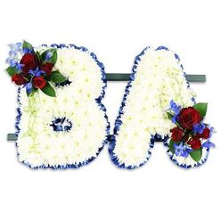 An elegant, personalised memorial arrangement shapes the uppercase letters B and A with careful floral craftsmanship, a style we prepare regularly for funerals and commemorations across Queensbury and nearby Harrow. Each letter is densely covered in hundreds of small white chrysanthemum florets, layered to form a soft, cloud-like surface that looks and feels cushiony beneath the hand. The silhouettes are cleanly edged with a ruffled royal blue satin ribbon that both defines and dignifies the letters, the deep blue offering a steady contrast to the luminous whites. A vibrant accent cluster sits on the B's upper left curve and a matching one on the A's lower right: rich, velvety red roses in varied stages of opening, interspersed with tall, electric-blue delphinium spikes and smaller blue florets, the cool tones striking against the warmth of the roses. Lush dark green foliage and delicate pale green trailing stems are woven through these clusters, introducing texture and a natural, slightly trailing line. The two initials are mounted side-by-side on a slim dark-green stand for stable display, photographed on a neutral white backdrop so every colour reads clearly. Prepared by Flower Delivery Queensbury for local services near Queensbury station, Kingsbury and Kenton, this composition balances tradition and personalisation - purity in the chrysanthemum, affection in the roses, and composed formality in the blue ribbon - offering a comforting, tactile visual message of remembrance.