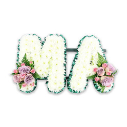 Set against a plain white backdrop, this elegant MA funeral letter tribute appears almost to float, its soft textures and quiet colours creating a sense of calm that would sit beautifully in a chapel in Queensbury or nearby Kingsbury. Both capital letters are crafted from dense clusters of pristine white chrysanthemums, each flower head carefully placed so there are no gaps, just a seamless blanket of petals. The surface looks cloud-like and gently tactile, as if you could run your fingertips across it and feel only cool softness. Surrounding the letters, a rich dark green satin ribbon folds into delicate pleats, outlining every angle and curve of the M and A. This defined border gives shape and strength to the airy white blooms, creating a striking contrast that still feels understated and respectful. At the lower left of the M and the lower right of the A, the design is softened with romantic sprays of pastel flowers. Pale pink and lilac roses mingle with tiny pink spray roses, their spiralled petals layered like fine silk. A few slender fern fronds curl outwards, adding fresh greenery and a light, natural texture that breaks the formality of the letters. The composition is carefully balanced and symmetrical, with each accent bouquet echoing the other in size, colour, and placement. There is no dramatic lighting or cluttered background, only gentle, even light that allows the details to be clearly seen. The tribute feels like a personal, intimate gesture, perfect for honouring a beloved Ma, Mama, or grandmother at a funeral or memorial gathering in the local area, where family and friends gather to say goodbye with quiet dignity.