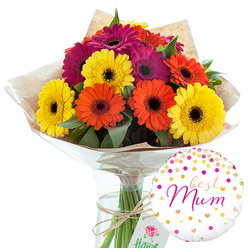 This image captures a joyful gerbera bouquet and balloon pairing, photographed against a clean white background that lets every colour sing, much like the bursts of colour you see in front gardens around Queensbury on a sunny afternoon. At the heart of the scene is a lush cluster of large gerbera daisies, their wide, flat petals radiating out in bright rings of yellow, orange, and deep magenta. Each bloom is fully open, with a contrasting dark centre that draws the eye and gives structure to the arrangement. The flowers are nestled among sprigs of deep green foliage, which weave between the heads and soften the outlines, suggesting movement and natural growth. The stems have been gathered by a skilled florist, wrapped first in a softly crinkled layer of light brown kraft paper and then in a sheath of clear, glossy cellophane that reflects subtle highlights. A band of natural twine secures the wrapping around the stems, its simple knot adding a handmade, thoughtful touch. The bouquet stands upright in a slim, transparent glass vase filled with water, allowing the viewer to see the straight green stems continuing down into the base like a tidy bundle. To the right-hand side, slightly lower than the flower heads, floats a crisp white foil balloon. Its surface is sprinkled with confetti-like dots and small hearts in pinks and metallic golds, picking up the tones of the flowers. At its centre, in elegant pink cursive, the words "best Mum" are written, clearly marking this as a tender, celebratory gift, ideal for Queensbury families honouring a mother or mother figure with a bright, modern floral surprise.