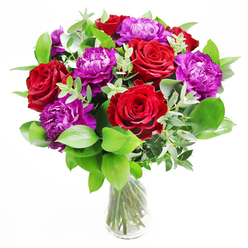 In this image, a sophisticated yet exuberant floral arrangement is presented in a simple, cylindrical clear glass vase, placed on a smooth, neutral surface that lets the colours sing. At the heart of the design are velvety red roses, each bloom unfurling in a tight, elegant spiral, their petals plush and saturated with colour. Woven between them are opulent purple peonies, generously ruffled and full, their rounded forms and layered petals giving the bouquet a sense of abundance and gentle luxury. A foundation of lush greenery encircles the flowers, with deep green leaves providing structure and light, silvery eucalyptus stems threading through the design. The eucalyptus leaves arc softly, adding a hint of movement and a cool, contemporary touch that contrasts beautifully with the classic romance of the roses. Light falls from one side, as if streaming through a window of a Queensbury home looking out toward local parks, casting soft reflections through the vase and highlighting the natural veining in each petal. The stems are neatly arranged and clearly visible through the water, reinforcing the impression of freshness and careful craftsmanship, as though prepared that morning for same-day delivery across Queensbury by an attentive neighbourhood florist. The imagined scent is a gentle blend of rose sweetness and green, slightly citrusy eucalyptus, the sort of fragrance that would subtly fill a hallway or dining room without overwhelming it. This bouquet feels perfect for celebrating love, marking an anniversary, or expressing admiration-a confident, polished floral statement with enough softness to make it feel personal and sincere.