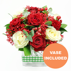 A rich, romantic bouquet of red and white roses is shown in crisp detail against a pure white backdrop, as if waiting to be placed on a dining table in a Queensbury townhouse. The arrangement is dominated by full, velvety red rose heads, their petals layered in loose spirals that suggest passion and warmth, balanced by softly glowing cream and ivory-white roses that bring a serene, elegant note. Between these classic blooms, tiny red filler flowers cluster like a cloud of sparkling confetti, their fine stems branching in all directions to create a light, airy halo of colour. Round, polished red hypericum berries punctuate the design, adding little globes of shine that echo the red roses but with a firmer, more structured form. Lush green foliage weaves through the bouquet: broad, glossy leaves provide a sturdy backdrop, while the muted, silvery-green eucalyptus leaves add movement and a contemporary twist, like greenery freshly cut from gardens off Honeypot Lane. The stems are gathered into a sleek, rectangular clear glass vase, where the clean lines of the container contrast beautifully with the softness of the petals. Around the centre of the vase, a green and white gingham ribbon is snugly wrapped, its cheerful check pattern lending a homely, country-kitchen charm that feels at once stylish and familiar. In the bottom right corner of the image, an orange circular label is overlaid with the words "VASE INCLUDED" in white capital letters, making it clear that this floral gift arrives complete and ready to display, perfect for same-day delivery in Queensbury when you want to express love, gratitude, or festive cheer without any extra fuss.