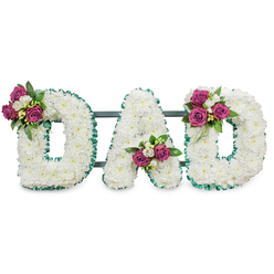 This memorial piece reads DAD in sculpted, three-dimensional letters entirely clothed in small, immaculate white chrysanthemums, their dense, cushiony heads blending into a seamless, peaceful surface. The white blooms carry a faint, clean scent that pairs with the soft visual texture to evoke purity and repose. Each letter's edge is crisply trimmed with an emerald-green, ruffled ribbon that frames the composition and lends a fresh, leafy tone reminiscent of nearby parks and hedgerows around Queensbury. Gently arranged accent clusters of rich magenta roses punctuate the composition: one nestles into the upper left curve of the first D, another settles softly in the lower central V of the A, and the last crowns the upper right curve of the final D. These roses-at different stages from tight bud to partially open-are coupled with tiny, white freesia-like blooms and deep-green foliage, adding contrast, scent, and a feeling of tender care. A muted dark-green or charcoal support bar discreetly links the letters from behind, suggesting an easel or grave-mounted frame ready for a service. The overall impression is one of composed affection and respectful farewell: a bespoke sympathy tribute that reads clearly in a chapel or church hall, and that carries the quiet, local sensibility of floral work prepared for families in Queensbury and neighbouring Kingsbury.