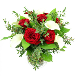 A round glass vase brims with a carefully balanced mix of deep red roses and elegant white calla lilies, captured against a bright white studio backdrop that lets the flowers speak for themselves. At the centre, several red roses are fully open yet still plush, their velvety petals forming tight spirals that build into generous, cup-shaped blooms in a saturated crimson shade. Among them, sleek calla lilies rise like sculpted accents, their smooth, waxy petals curling to form clean trumpet shapes, creamy white on the outside and gently embracing a pale golden spadix within. The bouquet is woven with abundant greenery that softens and enriches the overall shape: soft eucalyptus, with its rounded, blue-green leaves, adds a feathery, slightly cascading texture, while glossy, darker green foliage provides a dense, verdant base that cradles the roses and lilies. Clear water fills the cylindrical vase, revealing the neat bundle of stems and a subtle ribbed band near the bottom that adds a touch of refinement. Bright, even lighting picks out the sheen on each petal and leaf, making the reds more intense and the whites almost luminous, as if freshly prepared for delivery across Queensbury and nearby areas like Kenton and Kingsbury. The mood of the arrangement is one of poised celebration-equally suited to marking a special anniversary, honouring a milestone birthday, or simply bringing a sense of romantic elegance to a living room or restaurant table in the heart of Queensbury.