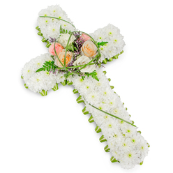 Set against a spotless white backdrop, a traditional Christian cross made entirely of flowers appears both solid and tender, like a symbol of faith translated into petals. The body of the cross is generously covered with countless small white chrysanthemums or similar dainty blooms, each head carefully angled so that together they form a smooth, velvety surface, almost like freshly fallen snow. A slim yet striking trim of bright green foliage traces the edges, running continuously around the upper arms and straight down the stem, emphasizing the clean geometry of the tribute and adding a fresh, garden-like feel. At the central junction of the cross, a raised cluster of larger blooms becomes the heart of the design: roses in soft peach, pale blush, and creamy white, their layered petals opening in quiet beauty. These sit amongst wisps of airy ferns, slender strands of looping grass, and small accents of fine purple flowers that gently deepen the palette. The arrangement is lit softly and evenly, with no drama in the lighting, allowing the natural textures and subtle colour shifts to speak for themselves. It feels like something a local Queensbury family might see resting near the altar of a nearby church or travelling with them from a home along Honeypot Lane to a final service. Composed with the care of an experienced florist, this funeral flower cross carries a mood of serenity, consolation, and enduring love, ideal for saying farewell while reflecting both Christian faith and a deep, personal respect for the life being remembered.