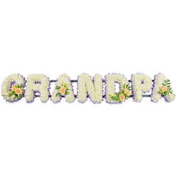 A carefully crafted floral tribute spells GRANDPA in bold, upright letters, set horizontally as though resting gently before a funeral service in Queensbury. Each of the seven uppercase characters is densely packed with pristine white spray chrysanthemums, their countless petals forming a soft, cushiony surface that looks almost velvety to the touch. Hints of pale yellow at some flower centres lend a natural warmth, while the overall white expanse speaks of respect, remembrance, and a peaceful passing. Tracing the outline of every letter is a slim band of light lavender or lilac blooms, which create a gentle contrast, sharpening the silhouettes of the G, R, A, N, D, P, and final A against the stark white background. This lilac edge has the quiet calm of a soft evening sky above the rooftops near Queensbury Station.   

Several letters are embellished with small, harmonious sprays of accent flowers. The G features a prominent grouping of three to four peach-toned roses, some fully open, others still cupped in bud, combined with narrow white lily buds and polished green leaves. On the first A, a single peach rose with surrounding foliage is tucked into the flowers, adding a personal, intimate touch. The D holds another cluster of peach roses and greenery, reflecting the styling of the G to bring balance across the word. The closing A is finished with one more peach rose and fresh leaves, like a final whispered farewell. A thin, dark bar runs along the base, hinting at a discreet metal or foam frame that supports the entire arrangement, ready to be displayed at a local chapel or graveside. This personalised GRANDPA tribute feels both strong and tender, a floral message of love created for a beloved grandfather and the family who will remember him.