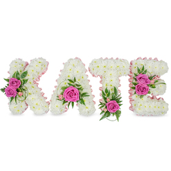 A lovingly made floral name tribute reading KATE, assembled from hundreds of tiny, immaculate white chrysanthemums to form large, three-dimensional letters that sit with reassuring solidity and a soft, clouded texture. Inside each letter, a pale pink satin ribbon follows the inner edges, lending a subtle blush that frames the white blooms and lifts the design under soft church lighting or muted chapel lamps. Hot pink roses are placed as expressive punctuation: two open roses soften the K's left arm, a single rose nestles in the A's lower centre, a vivid bloom anchors the foot of the T, and a pair of roses enliven the right side of the E. Accents of delicate pink spray flowers, ferny greens and variegated leaves weave among the roses, introducing cool, green notes and a faint, fresh scent that balances the sweetness of the petals. The letters are freestanding against a bright white background with gentle shadowing that highlights their dimensionality - an arrangement composed with the care of a seasoned florist. As Flower Delivery Queensbury, we often prepare this style for families arranging services at Queensbury's local churches or memorial chapels, and it reads with clarity at a distance while revealing meticulous handwork up close. The overall effect is tender and dignified: an understated but highly personal floral farewell that conveys love, remembrance and respect.