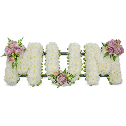 An elegant sympathy tribute arranged in large, three-dimensional letters reads MUM, each letter constructed from a dense mass of pristine white chrysanthemums that create a soft, textured surface reminiscent of freshly fallen snow. The overall effect is one of serene purity: the white blooms reflect a subdued light and form a calm backdrop for three artful accents - small clusters of soft lavender roses and pale pink rosebuds placed with intention on the upper left of the first M, tucked into the central curve of the U, and crowning the upper right of the final M. Bright green foliage, including delicate fern fronds and lighter green leaves, threads between the pastel roses and the chrysanthemums, adding contrast, movement, and the reassuring freshness of living stems. A dark green structural base, visible along the bottom edge, provides a subtle outline and support so the letters stand with dignity. The roses lend a velvety scent that mingles with the clean, faint scent of the chrysanthemums; together they convey sympathy, respect, and warmth. This arrangement feels hand-finished by an experienced Queensbury florist who understands local funerals and wakes - suitable for a chapel service or graveside near Kingsbury High Road or the quieter corners around Wembley - and it arrives as a composed, heartfelt message of remembrance and love in a difficult time.