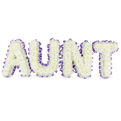 Carefully assembled in a small Queensbury studio close to the station, this personalised memorial piece spells AUNT in four bold, elegant letters, each densely packed with pristine white spray chrysanthemums. The chrysanthemums form a textured, cloud-like surface; their profusion of small petals softens the strong letterforms while tiny pale-yellow centres add the smallest, warm accents that catch soft daylight. Around every letter, a deep purple satin ribbon has been worked into a ruffled outline, the ribbon hugging curves and corners with neat pleats that frame the whiteness and lend the tribute a refined, finished silhouette. Grey shadowing beneath the letters reveals the depth of the frames and suggests the solid, three-dimensional construction of the display-designed to sit upright at a service, chapel or memorial table. A gentle green, floral scent arises from the chrysanthemums: clean and slightly dewy, calming for those nearby. The palette of white and purple reads as classic sympathy colouration-white for purity and remembrance, purple for dignity and heartfelt respect-so the arrangement feels like a dignified farewell. Prepared by experienced hands familiar with Queensbury, Kingsbury and nearby Wembley, this bespoke memorial is intended to communicate love, gratitude and the distinct place a beloved aunt held in family life, available as a considered tribute for wakes, funeral services or a quiet home remembrance.
