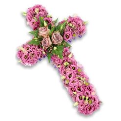 A refined floral cross arrangement appears centred on a clean white background, its shape clearly defined by a generous covering of fresh, densely arranged flowers. The entire cross is carpeted with lisianthus blooms in a harmonious medley of soft pinks, dusty mauves, and gentle purples, each blossom slightly ruffled at the edge, creating a plush, cushion-like texture as the eye travels along the arms. At the heart of the design, where the vertical and horizontal beams meet, three larger roses in muted rose-lavender tones open fully, their layered petals forming a tranquil focal point that draws attention and invites quiet reflection. Around this trio of roses, sprays of bright green fern and smaller, darker green leaves emerge between the petals, adding dimension and a fresh, living contrast to the romantic colour palette. Throughout the cross, tiny clusters of pink and lilac filler flowers, along with small white florets and pale green buds, are tucked carefully into the design, echoing the detail and care of a skilled local florist working in a studio just off Kingsbury Road near Queensbury. Subtle glimpses of deep purple ribbon or backing material appear along the edges, suggesting the underlying structure without overpowering the natural beauty of the blooms. The calm, balanced colours and the softness of the petals convey a message of peace, remembrance, and spiritual comfort. This floral cross would feel at home resting beside a chapel lectern or at the head of a casket, a thoughtful tribute chosen by family or friends to honour a loved one's life and faith within the Queensbury community.