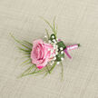 A delicately composed pink rose boutonniere lies against a warm, neutral beige fabric that could easily be the backdrop of a dressing table in a Queensbury home preparing for a special day. The rose itself is the undisputed focus, angled slightly to the left, its petals shaped in gentle spirals that move from vivid fuchsia around the outer edges into a softer, blush-pink heart. The bloom appears newly opened, with its centre still slightly furled, suggesting the freshness you'd expect from flowers delivered the same day across Queensbury. Surrounding the rose, specks of white baby's breath cluster in small sprays, like tiny confetti, giving the arrangement a light, romantic feel. Wispy, grass-like greenery extends from the back and sides, adding movement and a sense of natural flow that balances the structured form of the rose. At the base, a single deep green leaf wraps around the stems in a tidy collar, catching a few shining droplets of water that highlight the lushness of the foliage. The stems are carefully wrapped with a pale pink satin ribbon, its subtle sheen catching the light, and finished with a slimmer, darker magenta ribbon that forms a neat bow, adding a refined flourish. The soft, even lighting reveals every texture-the velvety rose, the airy gypsophila, the smooth ribbon-while the beige, linen-like background keeps the focus entirely on the flowers. This boutonniere feels made for a groom or prom guest heading out from Queensbury station, a small but meaningful expression of affection and celebration.