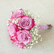 Laid gently on a neutral, woven beige backdrop that recalls the calm interiors of homes around Queensbury, this small bouquet radiates refined romance and careful artistry. Several bi-colour roses form the centrepiece, each bloom unfolding from a cool, powdery lavender or light purple heart into vivid magenta-pink edges, as though the tips of the petals have been brushed with rich fuchsia paint. The petals curl softly outward, creating layered rosettes that feel both modern and timeless. Threaded generously between the roses are clouds of baby's breath, their tiny white blossoms and slender green stems softening the vivid colour of the roses with a veil of delicacy and innocence. The stems are expertly bound in a deep purple satin ribbon, smooth and slightly glossy, which hugs the handle in immaculate, even folds. Over this, a fine strand of white faux pearls winds gracefully in a spiral, each bead catching the light to create a subtle, luxurious shimmer. The bouquet is photographed on a diagonal, the pearl-wrapped handle pointing to the right, hinting at movement, as though it has just been lowered from the hand of a bridesmaid stepping out of a wedding car on a quiet Queensbury side street. The mood is one of poised celebration: intimate rather than grand, but filled with feeling. You can almost imagine the soft, sweet perfume of the roses mingling with the clean, airy scent suggested by the baby's breath. Crafted with the kind of attention to detail you would expect from a trusted local florist, this bouquet feels perfect for weddings, proms, or special deliveries across Queensbury when words alone are not enough.