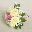 Nestled on a light beige linen-a fabric reminiscent of the calm interiors found in Queensbury's charming event spaces-this elegant bouquet radiates classic romance and modern flair. The standout features are its five creamy white or pale yellow roses, each delicately blossoming in a spiral of soft petals, while one vibrant magenta-pink rose sits slightly off-center, providing a striking focal contrast. Interlacing sprays of baby's breath lend a light, airy quality, softening the composition and evoking gentle spring breezes felt in parks near Queensbury. Rich, emerald-green leaves peek from beneath, framing the bouquet in fresh vibrancy. The stems are artfully bound in a sleek pink ribbon, its texture and hue harmonizing perfectly with the magenta rose. Spirals of tiny pearls embellish the ribbon, gleaming quietly under diffused daylight-a subtle nod to sophistication. The bouquet is aglow with freshness and fragrant charm, ideal as a bridesmaid's or smaller bridal bouquet for ceremonies celebrated around Queensbury. Every element speaks of personal touch and artistry, crafted for occasions where elegance and heartfelt joy are cherished.