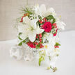 A romantic, rounded wedding arrangement of snowy lilies and sumptuous red roses sits gracefully in a simple white woven container, its design echoing the relaxed yet elegant character of Queensbury gatherings. The lilies, a creamy ivory white, stretch open like stars, each petal curved and smooth, inviting the eye inward to their softly dusted stamens. Nestled beside them, classic red roses unfurl in lush spirals, their petals layered like silk, bringing warmth and passion to the composition. Between these focal blooms, tiny white gypsophila clusters float like wisps of cloud, easing the transition between bold red and pure white. Glossy hypericum berries peep out in clusters, their rounded forms catching the light like little jewels, adding a cheerful, celebratory note. The bouquet feels carefully choreographed yet relaxed, as if a skilled florist has taken the time to listen to a couple's story and translate it into flowers. Gentle greenery frames the entire display, soft foliage arching around the blooms without ever stealing the spotlight. You might imagine this arrangement placed at the heart of a wedding table in a local Queensbury venue, or carried into a family celebration just off Honeypot Lane, its fragrance a subtle blend of lily sweetness and fresh rose. The overall impression is one of thoughtful craftsmanship and heartfelt emotion: an arrangement created not just to look beautiful in a photograph, but to feel meaningful in real life, for couples and families marking engagements, anniversaries, or intimate ceremonies across the Queensbury area.