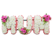 A thoughtfully crafted standing tribute spells the word MUM in three connected capital letters, photographed against a clean white background so every detail reads with calm clarity. Each letter is built from dense, snow-white chrysanthemums whose small, feathery petals form a plush, even surface - the familiar texture of sympathy florals that feels both gentle and resolute. A soft, ruffled trim of pale pink ribbon follows the outer edges of each letter, warming the composition with a tender blush that contrasts the pure white blooms. Between the letters a dark green support frame can be glimpsed, practical and discreet, holding the tribute upright for viewing at a service or graveside. The arrangement is brightened with three small clusters of fuchsia-pink roses - one tucked into the upper left of the first M, another nested in the curve of the U, and a third placed on the upper right of the second M - their velvety petals and deep colour offering intimate points of affection across the display. Lush fern-like foliage and glossy reddish-orange hypericum berries are woven into those posies, adding leafy texture and little jewel-like accents that catch the light. In soft morning light the chrysanthemums exhale a clean, subtle scent while the roses lend a faint, velvety perfume; together the piece reads as respectful, comforting, and lovingly composed. As a Queensbury florist I often prepare this style for local memorials and wakes near Queensbury station and the Parade; its traditional palette of white and pink communicates purity, remembrance, and enduring love in a form meant to be seen, touched, and remembered.