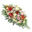 A dignified double-ended coffin spray is shown against a clear white background, its long, symmetrical form designed to be admired from every angle, much like those arranged for tender farewells in Queensbury's funeral homes and churches. The central line of the spray is anchored by vivid red Oriental-style lilies, their large, star-shaped blooms opening outward with a sense of quiet strength and solemn beauty. Around these striking flowers, a soft halo of cream and blush-pink roses is carefully placed, some still in tight buds and others fully unfurled, creating a gentle rhythm that speaks of love, respect, and the passage of time. Pale pink spray carnations ripple through the design, their ruffled petals lending a delicate, cloud-like texture that softens the stronger lines of the lilies. Between the larger flowers, small filler blossoms in light lavender and muted purple tones add fine detail and depth, preventing the eye from resting in any one place for too long and encouraging a slow, contemplative gaze. The entire composition is held within a cradle of deep green foliage: broad, glossy leaves form the main structure, while finer, trailing greenery spills slightly beyond the edge, giving a natural, unforced finish. The colours-rich reds, soothing creams, gentle pinks, and cool purples-combine to create an atmosphere of peaceful remembrance, suitable for a final tribute travelling from a family home near Queensbury Station to a nearby chapel. This carefully balanced spray conveys heartfelt condolences and offers a comforting presence during moments of loss and reflection.