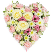 A beautifully composed heart-shaped floral tribute fills the frame against a flawless white background, its design echoing the tenderness and quiet strength often seen at remembrance services in Queensbury. The heart is densely packed, with every space thoughtfully covered in fresh blooms that blend soft pastel tones with deeper accents. At the centre and slightly off to one side, several large roses in shades of cream to pale buttery yellow unfold in graceful spirals, their velvety petals suggesting calm reassurance and unconditional love. Around and between these roses, a generous mass of pale pink carnations creates the main body and outline of the heart. Their ruffled, layered petals form a soft, cushion-like texture, offering a visual sense of comfort, as though the flowers themselves are holding the memory of a loved one. Threaded through this pastel base are bright white spider chrysanthemums, identifiable by their many thin, spiky petals radiating from greenish centres. They introduce lively texture and crisp contrast, balancing the arrangement so it feels both light and substantial. Clusters of deeper magenta-pink lisianthus are placed with care, their bell-shaped blooms adding a note of depth and quiet intensity, reminiscent of heartfelt stories shared after a service in nearby homes and streets off Kingsbury Road. Subtle hints of fresh green foliage peek through, keeping the tribute natural and fresh, as if it has just been arranged by a skilled local florist. At the very tip of the heart, a slim pink ribbon emerges beneath the flowers, a discreet detail that indicates this is a carefully finished funeral or sympathy tribute. Overall, the arrangement radiates compassion, remembrance, and enduring love, making it a fitting floral heart for honouring someone special within the Queensbury community.