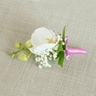 A delicate orchid boutonniere lies horizontally on a softly textured, oatmeal-coloured linen background, the kind of neutral fabric you might see on a groom's suit fitting table in a Queensbury bridal studio. At the centre, a single pristine white Phalaenopsis orchid opens its broad, velvety petals, their pure white surface catching the gentle, even light. The throat of the bloom glows with soft yellow and faint touches of pale pink, adding quiet warmth and depth. Nestled closely around the base of the orchid are tiny, cloud-like clusters of white baby's breath, each miniature flower forming a misty halo that softens the design and gives it an airy, romantic feel. A few slender, vibrant green leaves peek out from behind, offering a crisp contrast to the white petals and lending a fresh, garden-picked character that feels right at home after a stroll through nearby Queensbury Park. To one side, several lime-green orchid buds sit tightly closed along a slim stem, hinting at new blooms yet to come and symbolising hope and new beginnings, so often at the heart of local weddings and proms. The stems are carefully wrapped and bound with a slim length of bright fuchsia pink satin ribbon, tied into a neat, elegant bow whose lustrous sheen adds a celebratory pop of colour against the neutral cloth. Soft lighting gently highlights every texture-the smooth orchid petals, the feathery baby's breath, the subtle weave of the linen-creating a calm, intimate mood. This refined floral accessory feels perfectly suited to a groom's lapel, a prom night in Queensbury, or any formal celebration where understated elegance and careful craftsmanship are cherished.