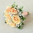 Nestled horizontally on a subtly textured, pale beige canvas, this bridesmaid bouquet embodies the romance and refinement that echoes through Queensbury's wedding venues. The heart of the arrangement showcases seven to eight lush, fully bloomed roses in a dreamy palette of peach, apricot, and blush orange-each petal rendered in exquisitely spiraled layers, softly illuminated by gentle natural light. Clouds of tiny white baby's breath fill the spaces between each rose, contributing a lightness that balances the richness of the primary blooms, while deep green rose leaves discreetly peek from beneath, adding a touch of woodland tranquillity drawn from nearby parks. The expertly rounded shape and compact arrangement reflect the careful hands of a Queensbury florist with a deep appreciation for classic bridal design. The stems are gracefully wrapped in a hand-pleated, coral-peach satin ribbon, further adorned with a winding row of delicate white faux pearls-evoking a timeless elegance reminiscent of traditional ceremonies at Stag Lane or community celebrations on Mollison Way. The very base reveals freshly cut stems, lending a sense of authenticity and artisanal touch. With its balanced harmony of color and texture, this bouquet is perfect for weddings, vow renewals, or heartfelt celebrations across Queensbury, capturing the joy, hope, and enduring beauty of life's sweetest occasions.