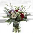 This stunning bouquet is a harmonious blend of contrasts, thoughtfully assembled in a local Queensbury studio for celebrations great and small. Deep crimson roses offer boldness and warmth, their lush petals catching the natural light that pours in across local neighborhood windows. Creamy white gerberas, each with a rich brown center, provide a classic yet lively touch, reminiscent of morning markets in Queensbury. The addition of pale lilac lisianthus-some still in elegant bud-introduces a delicate, contemporary softness, weaving promise and serenity into the composition. Graceful branches of eucalyptus fan outward, their round, silvery leaves dancing lightly above clusters of petite, ivory chrysanthemums that gather texture like pearls in a shell. At the bouquet's foundation, broad, sculptural leaves frame the scene with polish and depth, while fresh green stems rest visibly within a clear glass vase, immersed in crystal water. The scent, a soft mingling of pure rose and crisp eucalyptus, brings to mind new beginnings-whether welcoming a newborn, marking a milestone along Kenton Road, or sending a note of comfort. Crafted for Queensbury's diverse and vibrant community, this arrangement is both uplifting and elegant, designed to cradle beauty and sentiment in perfect balance.
