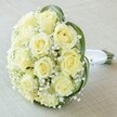 This close-up, high-angle composition presents a captivating bridal bouquet, thoughtfully created by a local florist in Queensbury. At its core, ten to twelve roses in velvety shades of pale yellow and soft cream cluster tightly, their petals arranged in graceful spirals, hinting at the beginnings of bloom. Among them, a lavish scattering of baby's breath dots the landscape with minute, snowy blossoms, contributing a gauzy, ethereal air that floats above the roses like mist after rainfall in Kingsbury's parks. Glossy arcs of rich green foliage encircle the bouquet, providing a fresh, modern accent that highlights and protects the delicate heart of the arrangement. The bouquet's stems, neatly gathered and secured by a band of pure white satin ribbon, are poised at the lower right, suggesting anticipation for a moment of celebration-a wedding procession, an anniversary toast, or a heartfelt proposal in the heart of Queensbury. Resting on an understated, neutral background, this composition speaks to the enduring elegance and romance of true craftsmanship, bringing the purest floral beauty to unforgettable events throughout the local area.