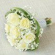 There's a quiet, radiant beauty in this bridal bouquet as it sits atop a softly textured, light beige surface, evoking an intimate celebration in the heart of Queensbury. Plush creamy roses, some tinged with gentle yellow, open in graduated layers-like promises unfolding-each petal reflecting the subtle glow of midday light streaming through local gardens. Dreamlike clouds of white baby's breath encircle and intermingle with the roses, adding a feathery delicacy reminiscent of a gentle early spring breeze along local footpaths. Elegant, looping blades of glossy green bear grass sweep gracefully through the bouquet, creating a modern, fluid silhouette that glimmers with each turn. Neatly gathered stems are swathed in luminous pale silver ribbon, the smooth satin finish embraced by neat rows of shimmering white pearls-a tactile nod to tradition and care. The natural cut ends peek just beneath, alive with the promise of freshness, as if only just delivered from a local Queensbury florist for a wedding at Roe Green Park or an anniversary tea shared at home. This bouquet brims with a sense of hope, sweetness, and devotion, crafted to elevate the most treasured moments and speak gently to the heart.