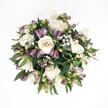 Captured from a bird's-eye view against a plain, luminous white background, this rounded sympathy bouquet appears calm and composed, as if gently gathered between caring hands. At its core, a cluster of creamy white roses opens in elegant spirals, petals curling back from soft ivory centres that hint at the faintest blush of peach. Some blooms are wide and generous, fully open to the light, while others remain partially closed, holding their shape in a way that feels protective and tender. Intertwined among the roses are slender stems of purple alstroemeria buds, their tapered forms flushed with deep lavender and violet at the tips, blending into pale green closer to the stems. Many of these buds are still tightly wrapped, suggesting the quiet promise of future blossoms, while a few show slender glimpses of patterned petals within. Wisps of delicate white baby's breath drift between the larger flowers, their tiny clustered blossoms adding a gossamer softness, like a fine veil laid over the arrangement. Surrounding this gentle interplay is a halo of rich green foliage, the leaves broad, glossy, and fresh, cradling the lighter blooms and giving the design a sense of structure and support. The overall composition is compact, spherical, and beautifully balanced, ideal for offering condolences in a subtle yet heartfelt way. One can imagine this bouquet resting on a table in a Queensbury home, perhaps near Queensbury Circle or close to local gardens, bringing a quiet sense of solace. The serene harmony of white, purple, and green creates a peaceful presence suited to times of remembrance and reflection.