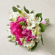 A romantic hand-tied bouquet is captured resting on a soft, light beige fabric, its gentle linen weave giving a calm, natural backdrop that allows every flower to shine. Dominating the design are plump hot pink peonies, fully opened so their many ruffled petals create a plush, cushion-like heart at the centre, with hints of deeper pink shading toward the middle. Woven among them, crisp white alstroemeria blooms unfurl gracefully, each narrow petal edged in cream and subtly streaked with fine maroon lines and speckles that lend a wild, almost woodland charm. Slender green buds rise between the blossoms like exclamation marks, adding height, texture, and a sense that more flowers are just about to burst into life. Around the edge, glossy dark green foliage curves protectively, deepening the colours and giving the bouquet a well-balanced, domed silhouette. The stems are gathered firmly together at the base, their clean green lines visible where they peek from beneath a pale pink ribbon tied snugly around them, the knot tidy and deliberate in that classic bridal style. The bouquet feels like it could have been prepared early in the morning by a Queensbury florist, ready to be carried to a wedding at a nearby venue or delivered to a home near Kingsbury Circle. The atmosphere is fresh, cheerful, and slightly nostalgic, with the peonies suggesting abundance and the alstroemeria adding lightness, a combination perfect for marking engagements, anniversaries, or any special day when you want to send a message of affectionate joy across Queensbury and the surrounding streets.