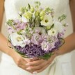 Like the whisper of an early spring breeze flowing through Queensbury's gardens, this bridal bouquet exudes quiet enchantment and refined beauty, thoughtfully captured in a close-up that reveals every detail. Creamy lisianthus blossoms unfurl in soft layers, their petals tender and inviting to the touch, nestled among clouds of pale lavender stock that lend sweet fragrance and a dreamy, mistlike texture to the design. Interspersed are new lisianthus buds-hints of unfolding beginnings-and the captivating, spiky radiance of deep purple allium crowns the base, introducing a playful architectural contrast. Dark green bear grass is woven with care, forming graceful arcs that frame the softer blooms and add a contemporary rhythm to the bouquet's silhouette. The bride's hands, polished in a gentle nude, cradle the stems lovingly, while a subtle glimpse of lace and satin from her dress blurs softly behind, reinforcing the pure, joyful mood of the day. The overall effect is ethereal and fresh, evoking the sensation of wandering through Queensbury's morning dew-every flower, every touch a testament to romance, hope, and skilled hands that gather beauty from local meadows and markets. An ideal bouquet for a bride cherishing a romantic, quietly confident celebration in Queensbury, artfully composed for heartfelt memories.