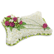 A rectangular pillow-shaped funeral tribute, photographed on a clean white background that throws a soft shadow beneath the arrangement, is densely crafted from hundreds of small, pristine white chrysanthemum florets to form a cloud-like, comforting surface. The chrysanthemums are tightly packed so the cushion reads as one serene plane of ivory petals, their matte texture and subtle scent suggesting peace and quiet. The edge of the pillow is neatly finished with a folded lime-green satin ribbon forming a delicate scalloped trim, adding a fresh, gentle frame and a whisper of colour against the white. In the upper left corner a compact cluster of deep magenta roses, velvety and richly saturated, sits alongside small white freesia blooms whose delicate trumpets bring a light floral fragrance and a hint of brightness. Darker fern fronds and varied green foliage cradle that cluster, creating depth and a living backdrop to the roses. Two slender, arching blades of bright green bear-grass sweep across the pillow in a graceful curve from the top cluster towards the lower right, introducing movement and leading the eye toward a single matching magenta rose placed near the lower right corner, which balances the composition like a gentle punctuation. The overall effect is one of tender craftsmanship and reverent calm: a traditional sympathy pillow meant to evoke restful sleep and quiet remembrance. As a local floral tribute suitable for services around Queensbury and neighbouring Kingsbury or Wembley, it reads as both an elegant design and a heartfelt gesture of consolation.