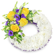 This sympathy wreath is shaped as a perfect letter 'O', a quiet, circular embrace of hundreds of small, pristine white spray chrysanthemums densely packed to form a soft, cloud-like band. From a florist's viewpoint the texture reads as calm and steady: the tiny multi-petaled heads sit snugly together, their matte white petals catching soft studio light and suggesting a gentle, powdery fragrance of summer evenings. Nestled on the upper left curve is a focused, heartfelt spray - several fully opened yellow roses in shades of butter and saffron, their petals spiraled inwards and lending a warm, uplifting note to the composition. Interwoven with those roses are deep royal-purple lisianthus (Eustoma), their ruffled, cup-shaped blooms creating velvet-like contrast; a handful of pale lavender buds and green-to-lavender Eustoma buds push through the cluster, adding depth and the sense of life in progression. Lush green foliage-glossy, rounded leaves with subtle variegation and delicate fern fronds-frames the accent and gives the wreath a natural, garden-fresh backbone. A narrow trim of dark purple mesh or crinoline peeks from beneath the white ring along both inner and outer edges, a discreet echo of the lisianthus hues that pulls the palette together. Set against a simple white background, the piece reads as reverent yet tender, an offering meant for memory and farewell. As a local Queensbury florist I often arrange this style for family tributes, imagining it placed in chapels near Queensbury station or at home, a visual promise of peace and compassionate presence.