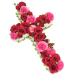 A carefully crafted funeral cross made from fresh roses is displayed against a bright, uncluttered white background, allowing its colours and details to stand out with quiet clarity. The cross itself is completely carpeted in roses, with velvety deep red blooms forming the main body and radiating a sense of devotion and lasting love. Among them, clusters of vivid fuchsia-pink roses add a gentle brightness, their soft, many-layered petals giving the arrangement texture and a touch of hopeful warmth. Tiny rosebuds in matching shades are nestled between the fully opened flowers, suggesting memories that are still unfolding and connections that remain. The outer edge of the cross is framed with a neat trim of delicate white blossoms, possibly spray chrysanthemums or miniature carnations, that create a luminous, cloud-like border and emphasize the familiar Christian cross shape. Slim strands of fresh green foliage and perhaps a subtle green ribbon appear just at the edge, giving the tribute definition and a natural finish. The composition is balanced and symmetrical, with the roses densely packed so that no gaps show, reflecting the careful work of an experienced florist. It feels like the kind of floral cross chosen for a family funeral in Queensbury, perhaps delivered to a local chapel or crematorium near Kingsbury and surrounding areas, where it would rest beside the casket or at the front of the service. The overall impression is one of gentle dignity and heartfelt remembrance, offering a visual expression of faith, love, and farewell.