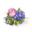 A delicate floral corsage or boutonniere photographed against a crisp white background, arranged with the measured hand of a seasoned florist to balance romance and modernity. At its heart sits a single, elegant rose, petals graduating from a gentle lavender-pink at the center to a vivid fuchsia at the outer edges, the soft velvety folds opening to suggest tender motion. Beside it a small cluster of indigo-purple florets, reminiscent of hydrangea or compact delphinium, catch the light with tiny bright blue and lime-yellow-green centers that act like summer sparks against the deeper petals. Around these focal blooms, lush greenery frames and supports the composition: broad variegated ivy leaves with deep emerald interiors and vibrant golden-yellow margins, slender silvery-green foliage evoking lavender leaves, and airy, featherlike sprigs of asparagus fern that lift the silhouette with breathy texture. A curled, striped leaf of green and cream introduces a sculptural line, drawing the eye across the piece. Below, an intricate dark purple mesh adds depth and a contemporary shimmer as it peeks out from beneath the flowers, while a short strand of lustrous white pearls at the lower right hints at a wristlet or elegant fastening. The overall scent is quietly floral and herbaceous, the surfaces ranging from plush rose petals to crisp variegated leaves and soft mesh. I imagine this worn at a Queensbury wedding, pinned to a lapel for a prom on The Broadway, or kept as a small keepsake - a tiny celebration of texture, colour and careful craft that feels both classic and current.