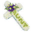 A cross-shaped floral tribute is laid out with quiet precision, the kind of piece you might see at a thoughtful memorial in Queensbury or a nearby church service. The main structure of the cross is densely covered in pristine white chrysanthemums, their compact, layered petals creating a smooth, almost quilted effect that feels soft and serene, like a blanket of fresh snow. Encircling the entire outline, a slim band of vivid green-either a ribbon or carefully positioned foliage-traces every edge, sharply defining the cross and adding a fresh, spring-like contrast. At the central point where the vertical and horizontal arms meet, a striking spray of flowers forms the heart of the tribute. Deep, velvety purple lisianthus, with gently ruffled petals, are nestled close to bright lime-green button chrysanthemums, whose lively tone lifts the whole composition. Dark green fern fronds arch gracefully around them, adding depth, texture, and a sense of natural movement, as though they had just been gathered from a shaded corner of a Queensbury garden. Along the vertical arm, a column of lime-green chrysanthemums runs down the middle of the white, creating a subtle visual rhythm. Fine, pale green wires or strands cross gently over this section, forming delicate lines that suggest care and craftsmanship rather than ornament for its own sake. The overall effect is one of reverent calm and soft colour, making this floral cross a fitting expression of sympathy and faith for funerals, memorial services, or graveside tributes across Queensbury.