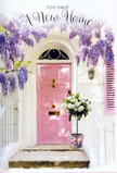 A quiet, sunlit doorway scene suggests the start of a new chapter in Queensbury, as if a bouquet has just been left by a thoughtful friend or delivered by a local florist to celebrate a move near Roe Green Park. The central focus is a pale pink front door, its surface softly matte and gently glowing as it catches warm afternoon light. Surrounding it, cascades of wisteria sweep down from above in plentiful clusters, their lavender and lilac blossoms layering over one another to form a romantic curtain of colour. Each drooping stem looks delicate and airy, casting a fine lace of shadow across the whitewashed wall, which provides a calm, bright backdrop. To the side, a pastel shutter painted in a matching blush tone quietly mirrors the door, creating a sense of balance and cohesion in the façade. On the doorstep, placed with intentional care, sits a grey tin bucket filled to overflowing with creamy white roses. The blooms are lush and full, some with centres still curled inwards, others fully open to reveal intricate spirals of petal upon petal. Soft green foliage peeks through the arrangement, giving a natural, garden-fresh feel that echoes the greenery of nearby Queensbury gardens. A pale pink ribbon is tied neatly around the bucket, its gentle sheen and relaxed bow adding a final stroke of tenderness. The entire vignette feels like a heartfelt housewarming card brought to life-serene, hopeful, and imbued with the comforting promise of welcome home for someone just settling into their new life in Queensbury.